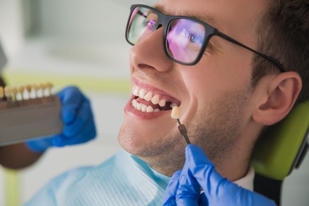 Dentist matching tooth shade for a dental implant crown restoration on a smiling male patient