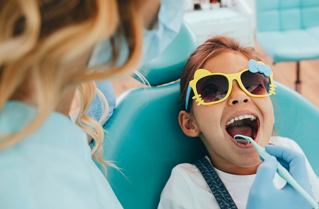 Young girl wearing sunglasses smiling during a dental exam with her dentist